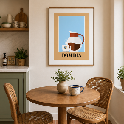 A framed art print featuring a minimalist coffee-themed illustration with the text 'BOM DIA' hangs on a beige wall in a modern kitchen setting with a wooden table and chairs.