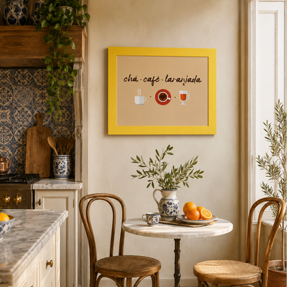 A framed wall art print featuring the Spanish phrase 'chá café lavandada' with simple illustrations of cups and a red plate, hanging in a warm, rustic kitchen setting above a small dining table with wooden chairs.