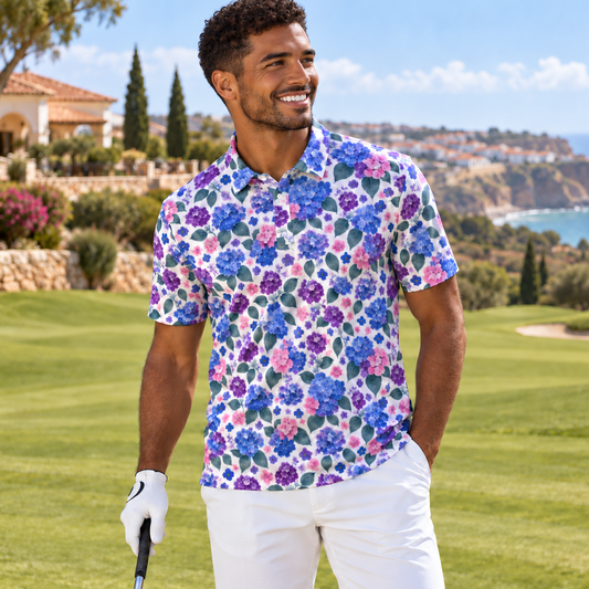 A man standing on a golf course wearing a short-sleeve button-up shirt with a colorful floral print in purple, blue, pink, and green, paired with white shorts and a white golf glove.