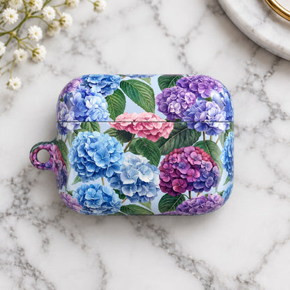 A rectangular hard case with rounded corners and a small hanging loop on the left, decorated with a floral print of blue, purple, and pink hydrangeas with green leaves on a pale background.