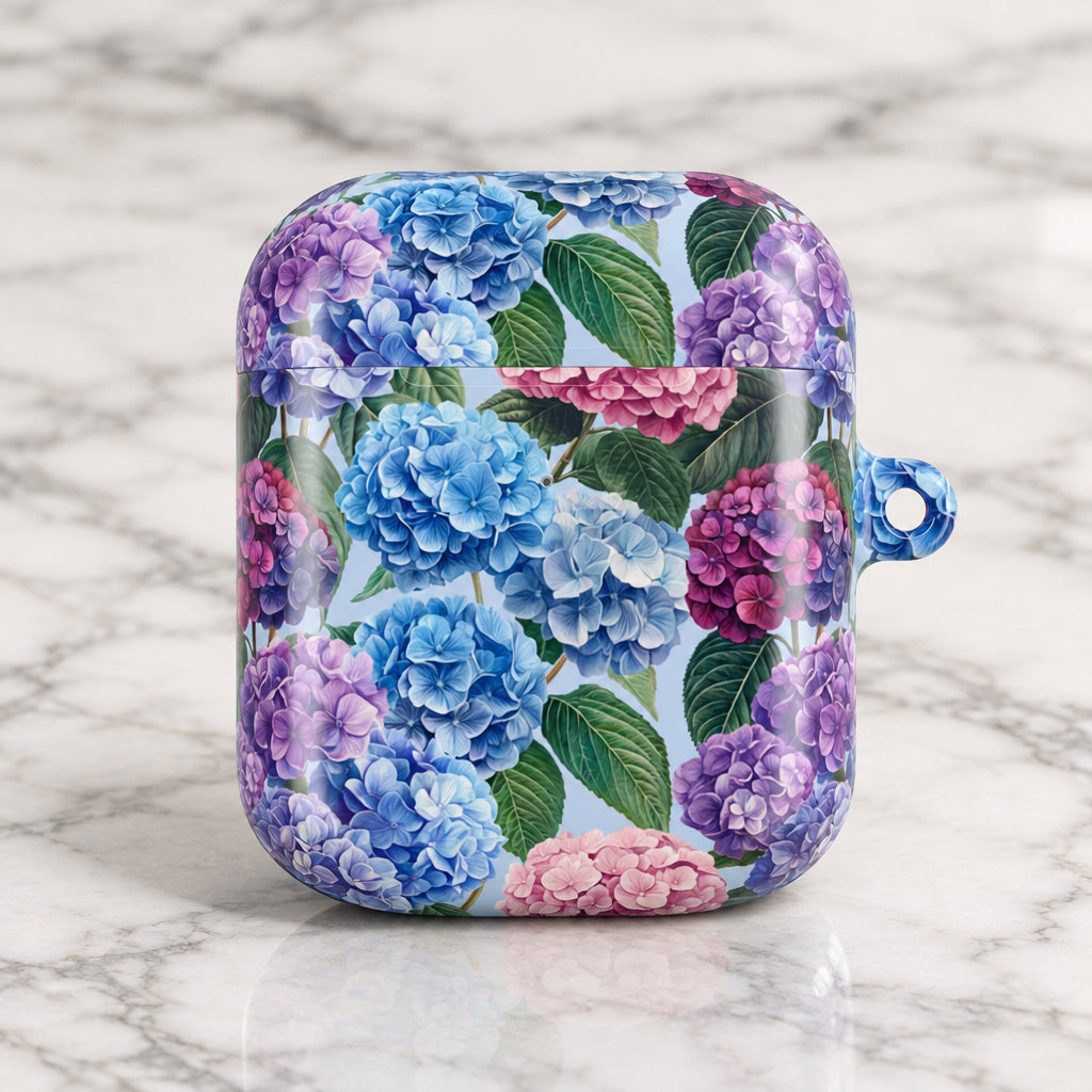 A protective case for wireless earbuds featuring a vibrant floral print of blue, purple, and pink hydrangeas with green leaves on a white background. The case has a small blue hanging loop on the right side.