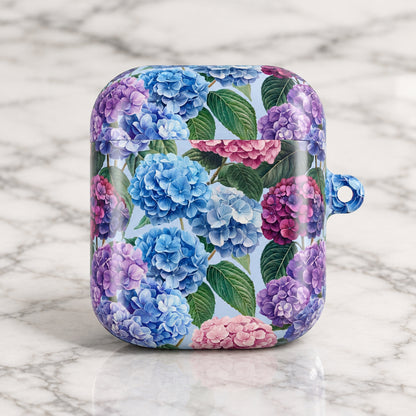 A protective case for wireless earbuds featuring a vibrant floral print of blue, purple, and pink hydrangeas with green leaves on a white background. The case has a small blue hanging loop on the right side.