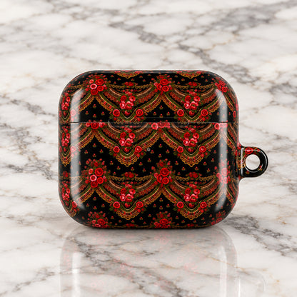 A protective case for an AirPods charging case, featuring a glossy black background with an intricate, symmetrical red and gold floral pattern, and a small metal loop on the right side.