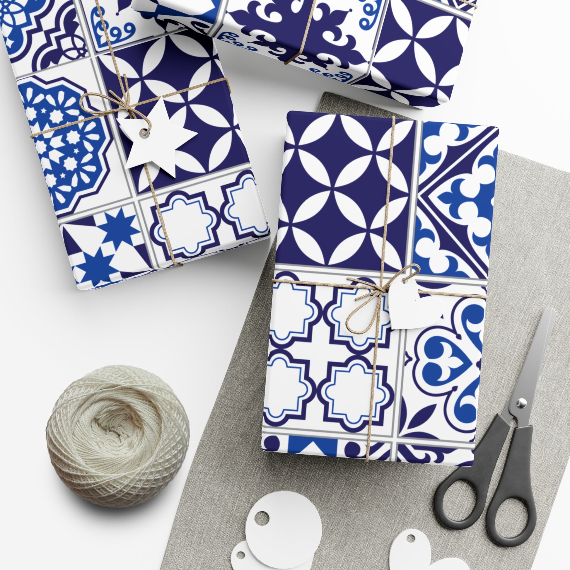 Gift boxes with blue and white tile patterned paper, scissors, and yarn on a white surface